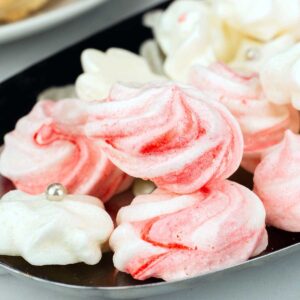 White and red swirl peppermint meringue cookies on a silver tray.