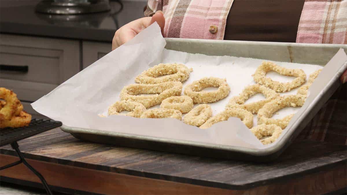 breaded calamari on a parchment lined tray for freezing.
