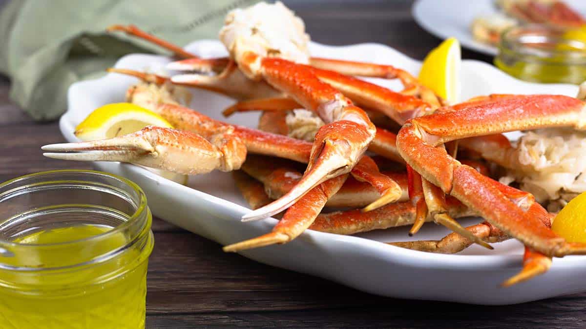 steamed snow crab legs on a white platter with lemon wedges and a jar of clarified butter.