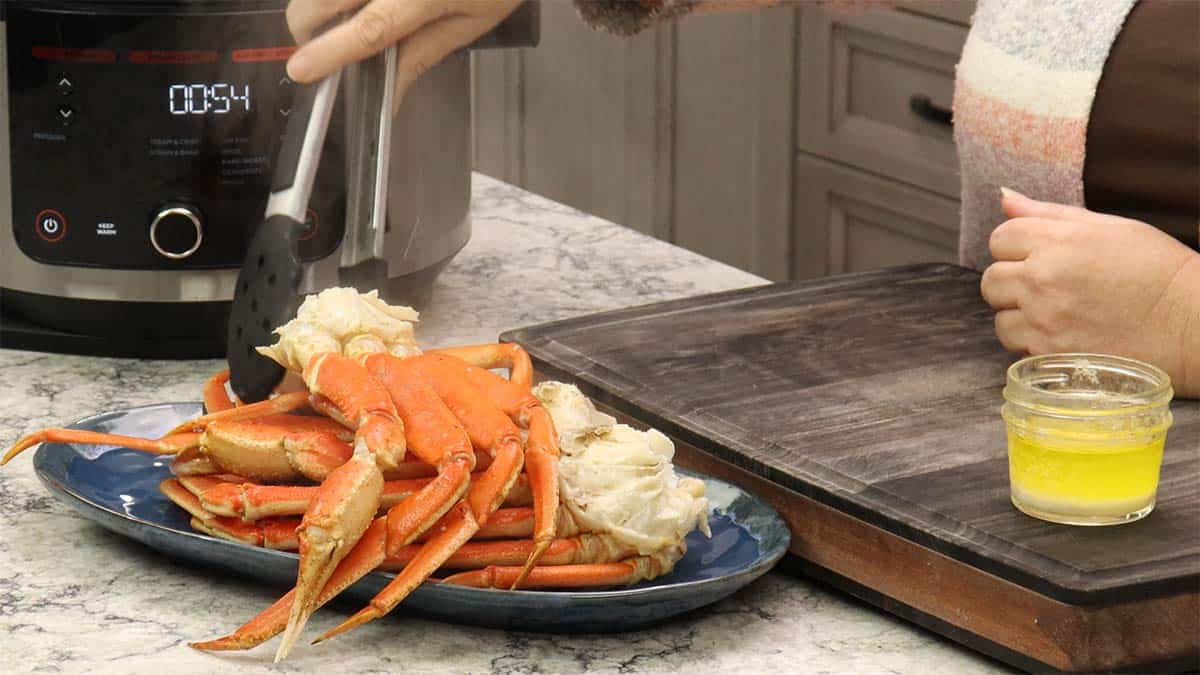 Using Tongs to remove the steamed snow crab legs and placing them on a serving platter. 