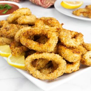 Air fryer calamari on a platter with lemon wedges and marinara sauce for dipping.