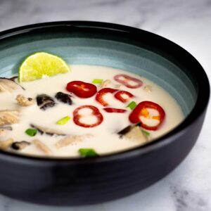 Bowl of coconut chicken soup with lime wedge.