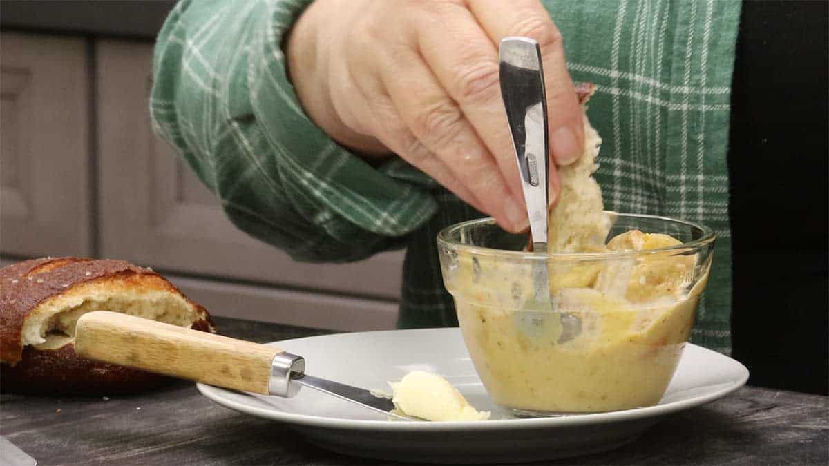 dipping the pretzel bun into a bowl of pickle soup.