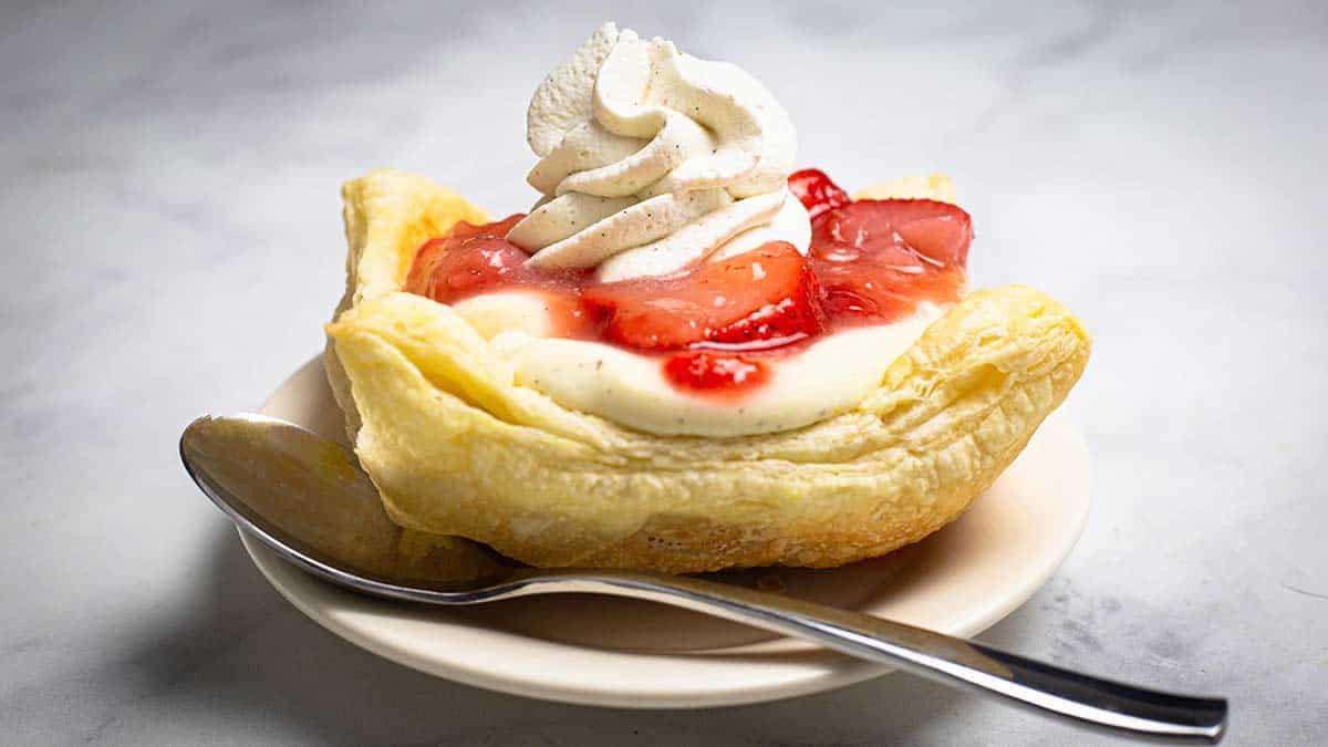 Puff pastry with cream and strawberries sitting on a white plate with a spoon.