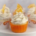 orange cupcakes sitting on a cupcake stand decorated with a buttercream swirl and a candied orange.
