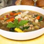 Summer Minestrone Soup in a white bowl on a yellow plate.