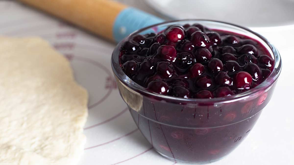 bowl of homemade blueberry pie filling sitting next to a rolled out pie crust.