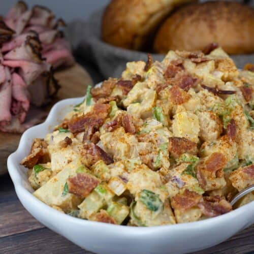 Smoked Potato Salad in a white serving dish garnished with fresh parsley and bacon.