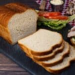 Homemade sandwich bread sliced on cutting board with turkey meat and condiments beside it for making sandwiches.