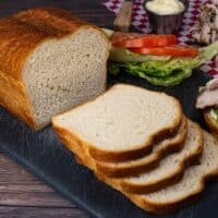 Homemade sandwich bread sliced on cutting board with turkey meat and condiments beside it for making sandwiches.