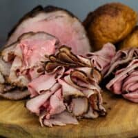Thinly sliced smoked bottom round with rolls in the background.