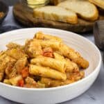 Chicken riggies in a white bowl with Italian bread slices behind it.
