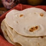 Homemade flour tortillas stacked in a basket lined with a red towel.