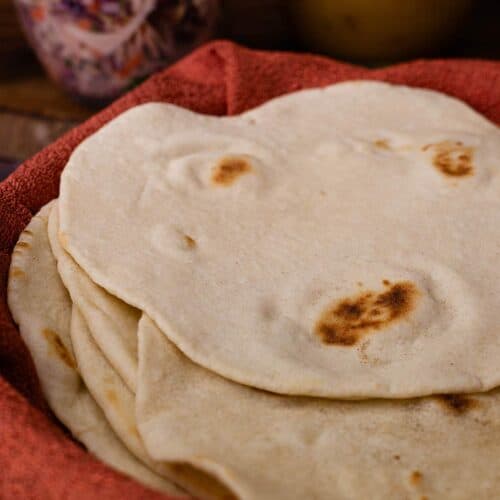 Homemade flour tortillas stacked in a basket lined with a red towel.