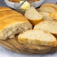 Loaf of Italian bread sliced on cutting board with butter in a bowl next to it.