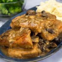 Pressure Cooked Pork Chops on blue platter with gravy and mashed potatoes.