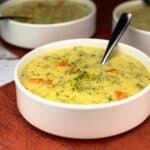 Broccoli Cheddar soup in a white bowl sitting on a orange/red napkin.
