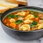 bowl of sausage and spinach tortellini soup with Italian bread slices to the left.