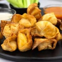 Buffalo Chicken Wontons on a black serving platter with blue cheese dressing, buffalo sauce, and celery.
