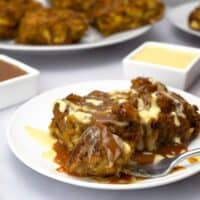 Pumpkin bread pudding on a plate drizzled with caramel and vanilla sauces.