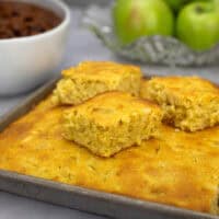 Apple cornbread with a few squares cut out of the pan and sitting on top of the rest of the cornbread.