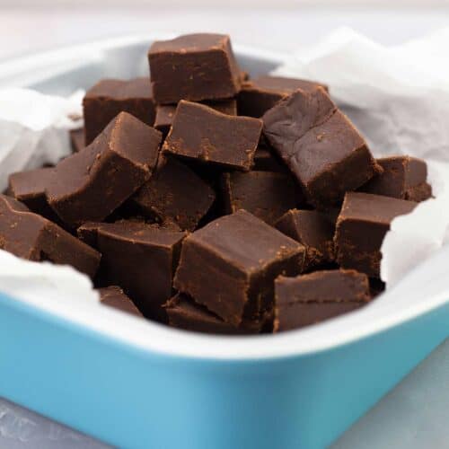 Chocolate fudge cut into squares in a blue pan with parchment.