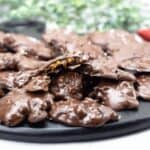 Black tray of pecan caramel clusters with one open showing soft caramel in the center.