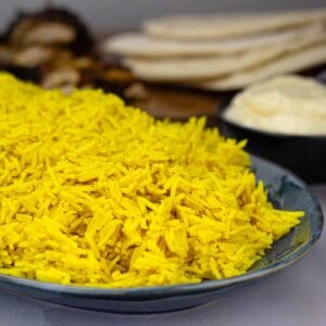 yellow basmati rice in a serving dish with shawarma wraps beside the dish.