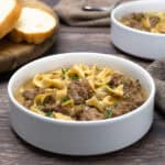 Two bowls of Swedish Meatball soup next to sliced bread and napkins with spoons.