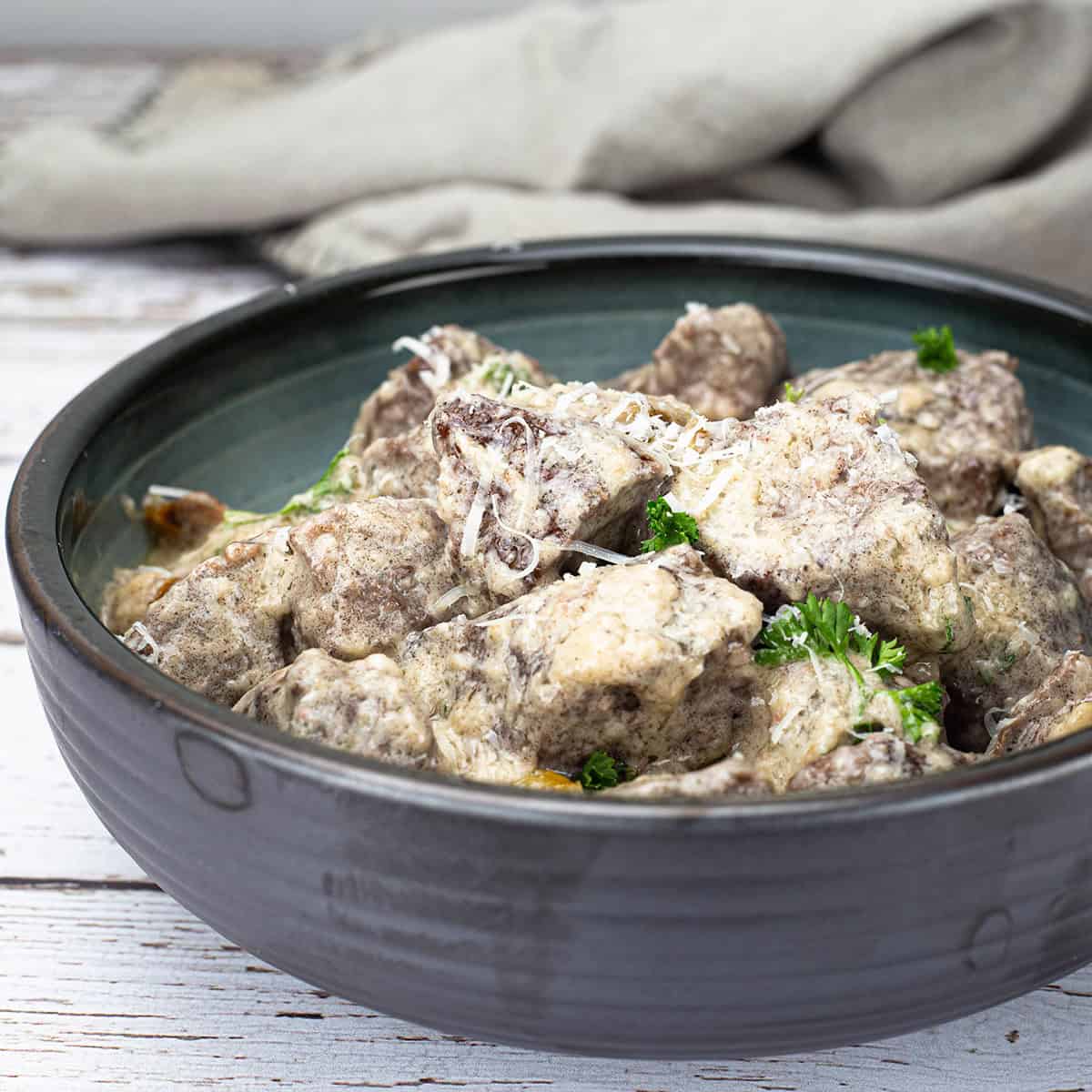 Garlic Parmesan bites in a dark bowl sitting on a table.