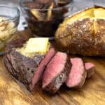 Sous Vide Sirloin sliced with a perfect medium rare center sitting next to a baked potato.