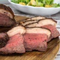 Sliced Rare Picanha roast on a wood cutting board with a salad behind it.