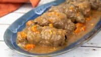 Beef Rouladen on a blue serving tray with gravy and carrots.
