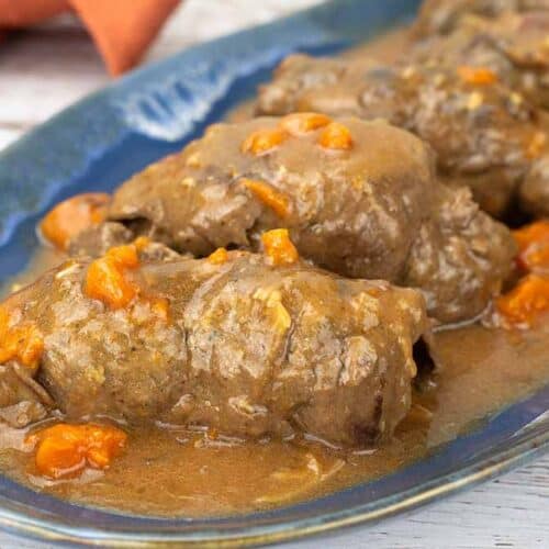 Beef Rouladen on a blue serving tray with gravy and carrots.