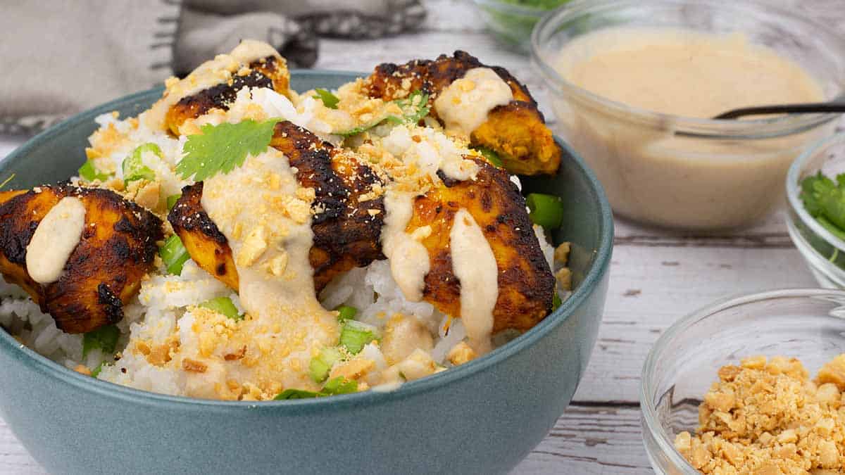 Chicken satay with rice and garnish in a blue bowl.