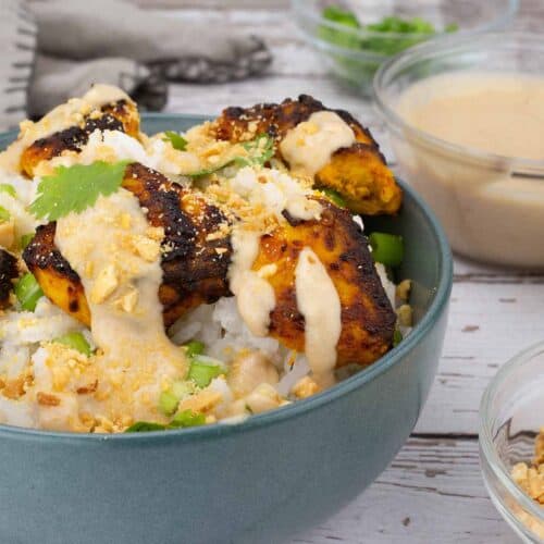 Chicken satay with rice and garnish in a blue bowl.