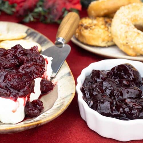 Cranberry Jelly in a white bowl next to bagels and cranberry preserves on top of cream cheese with crackers on a platter.