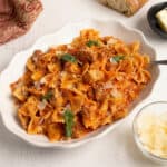 Square crop of Parma Rosa Pasta with Chicken and Sausage in a white bowl with creamy pink sauce, bow tie pasta, sausage, and chicken garnished with parmesan and basil.