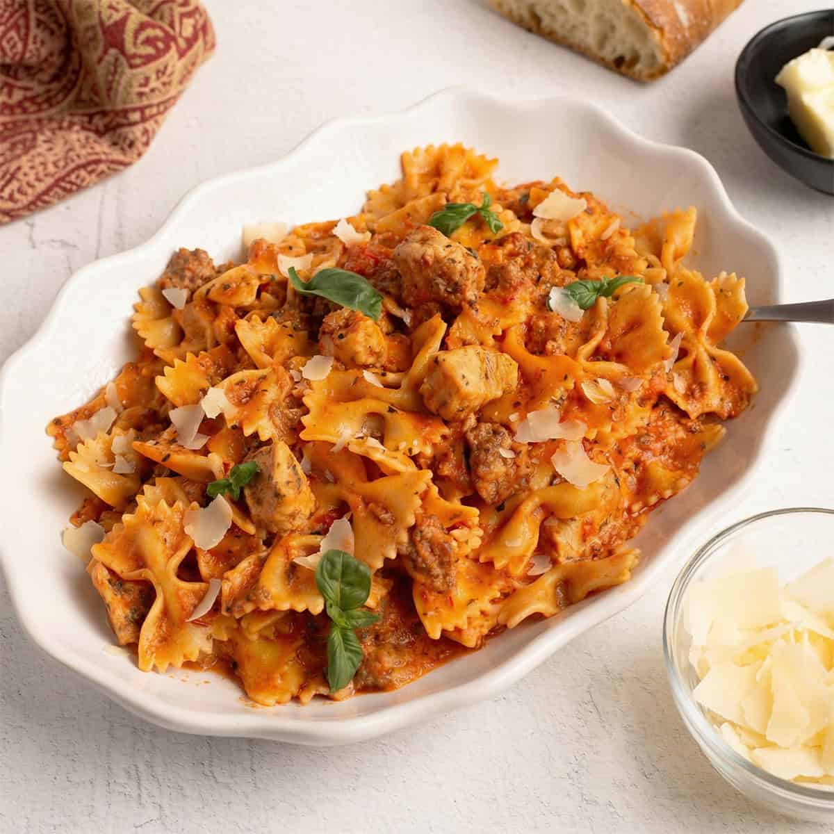 Square crop of Parma Rosa Pasta with Chicken and Sausage in a white bowl with creamy pink sauce, bow tie pasta, sausage, and chicken garnished with parmesan and basil.