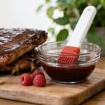 Raspberry BBQ sauce sitting next to ribs with text saying easy homemade raspberry bbq sauce.