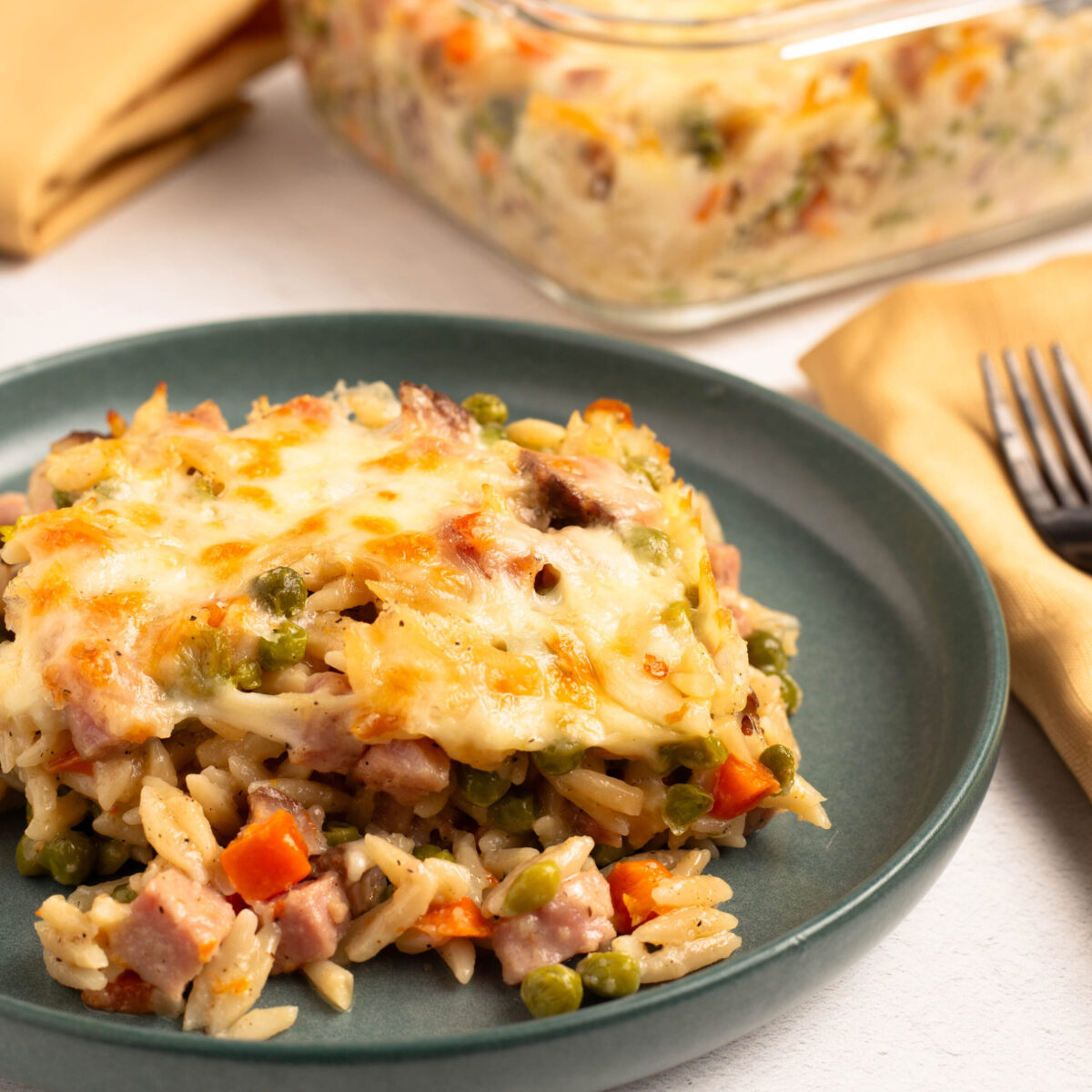 Ham and cheese pasta bake topped with bubbly golden cheese on a teal dinner plate