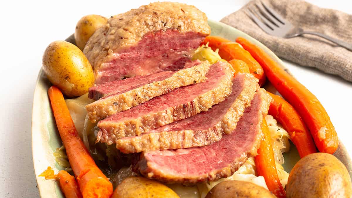 sliced Corned Beef and Cabbage with Potatoes and Carrots on a green platter.
