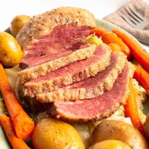 sliced Corned Beef and Cabbage with Potatoes and Carrots on a green platter.