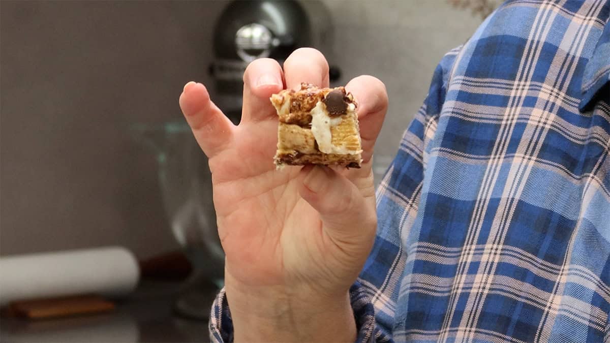 A hand holding a Cinnamon Toast Crunch bar broken in half, showing the gooey marshmallow and cereal texture inside