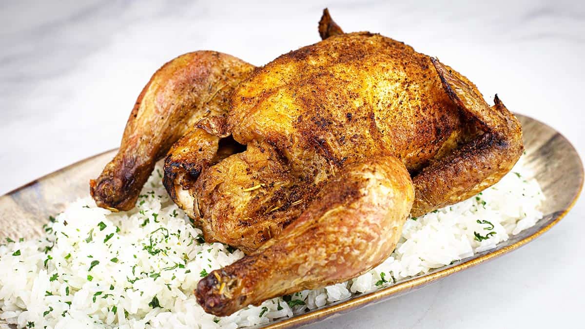 Whole air fryer cornish game hen with crispy seasoned skin plated on rice with parsley, wide landscape view.