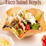 Pinterest pin titled Crispy Air Fryer Taco Salad Bowls showing a crispy tortilla bowl filled with seasoned ground beef, lettuce, tomatoes, cheese, olives, jalapenos, guacamole, and a drizzle of creamy taco sauce, with side bowls of toppings.