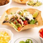 Crispy air fryer flour tortilla taco salad bowl filled with seasoned ground beef, shredded lettuce, diced tomatoes, shredded cheese, and a dollop of sour cream