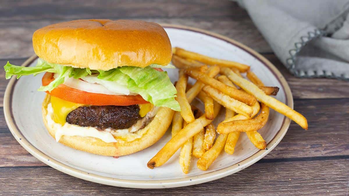 Juicy air fryer cheeseburger with melted cheese, crisp lettuce, and tomato on a toasted brioche bun, served with crispy french fries on a rustic plate.