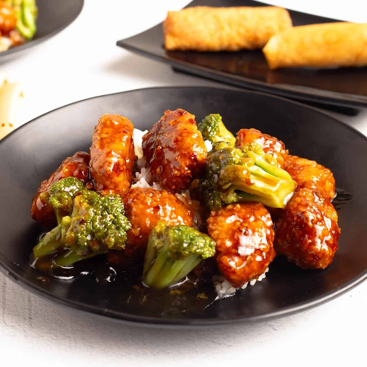 Close up of General Tso's chicken with crispy glazed chicken and broccoli served over white rice in a black bowl.
