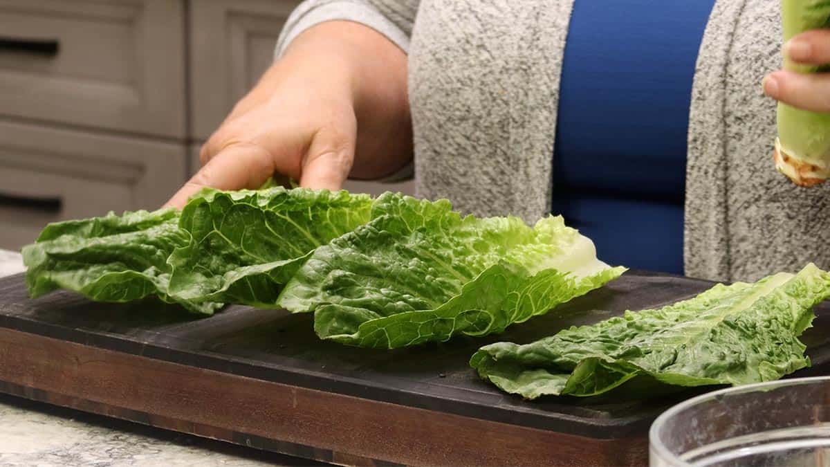 Hands arranging fresh romaine lettuce leaves on a wooden cutting board for plating Air Fryer Tuna Steaks.